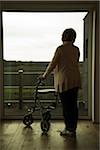 Senior woman using walker, standing and looking out of window, Germany