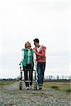 Teenage grandson with grandmother using walker on pathway in park, walking in nature, Germany