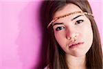 Close-up portrait of young woman with long, brown hair, wearing headband, looking at camera, studio shot on pink background