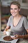 Portrait of young woman sitting in cafe with coffee cup and cellphone