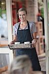 Young female waitress carrying tray of coffee cups in cafe