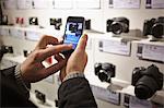 Mid adult man photographing camera's in shop display using smartphone