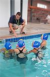 Four schoolgirl water polo players listening to teacher poolside