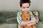 Portrait of young boy on sofa hugging teddy