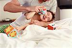 Father and young son playing with building blocks on bed