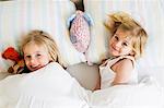 Portrait of two young sisters lying side by side in bed