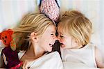 Portrait of two young sisters lying face to face in bed