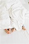 Young sisters feet sticking out of duvet on bed