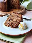 A whole Somerset apple cake with a slice on a plate in front with cream and honey