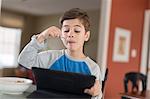 Boy looking at digital tablet whilst eating breakfast