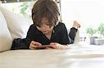 Young boy lying on sofa playing on hand held video game