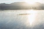 Rowing team rowing boat on still lake