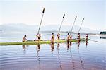 Rowing team with oars raised on lake