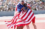 Track and field athletes wrapped in American flag on track