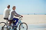 Senior couple riding bicycles on beach