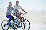 Senior couple riding bicycles on beach boardwalk