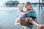 Senior man carrying wife on sunny beach