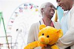 Senior couple with teddy bear hugging at amusement park