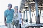 Senior couple laughing near pier at beach