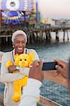 Senior woman with teddy bear posing for photograph at amusement park