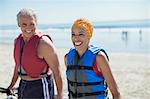 Enthusiastic couple in life jackets on beach