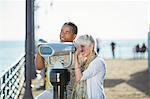 Senior couple using coin-operated binoculars on pier