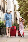 Mother and daughter pulling suitcases along pavement