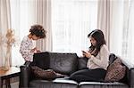 Two sisters sitting on sofa using digital tablet and cellphone