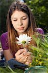 Teenage girl lying in grass looking at a daisy