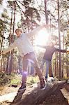 Twin brothers walking along fallen tree trunk in forest