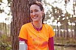 Mature woman runner with earphones taking a break in a forest