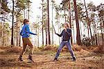 Twin brothers play fighting with sticks in forest