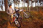 Twin brothers holding BMX bikes chatting in forest