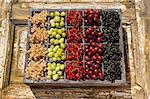 Assorted berries in an old wooden crate on a wooden surface (currants, gooseberries)