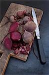 Several boiled beetroot, some peeled, on a wooden board with a knife