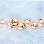 Apricot-coloured Christmas baubles in the snow