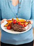A woman holding a plate of beef steak, tomatoes and sweet potato chips