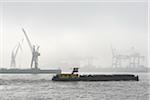 View of Harbour with barge and container cranes at loading docks in morning mist, Hamburg, Germany