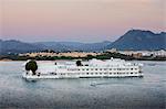 The Lake Palace Hotel, Jag Niwas, on island site on Lake Pichola in early morning with tourist boat leaving, Udaipur, Rajasthan, India