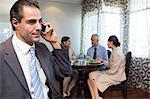 Businessman using cellphone with colleagues having meal