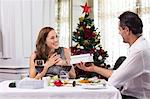 Man giving gift box to smiling woman in restaurant