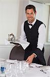 Happy waiter holding tray and setting table