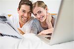 Happy couple on bed using laptop