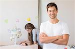 Happy mother watching over baby son in crib with father smiling at camera