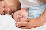 Happy father lying with baby son sleeping