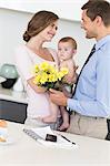 Father giving mother holding baby a bunch of yellow flowers
