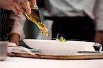 Chef adding olive oil to dish during service at working restaurant