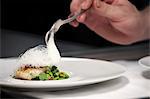 Chef plating up fish and broad bean dish during service at working restaurant