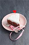 A slice of chocolate cake with grated coconut and a heart decoration