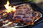 A T-bone steak in an aluminium tray on a barbecue